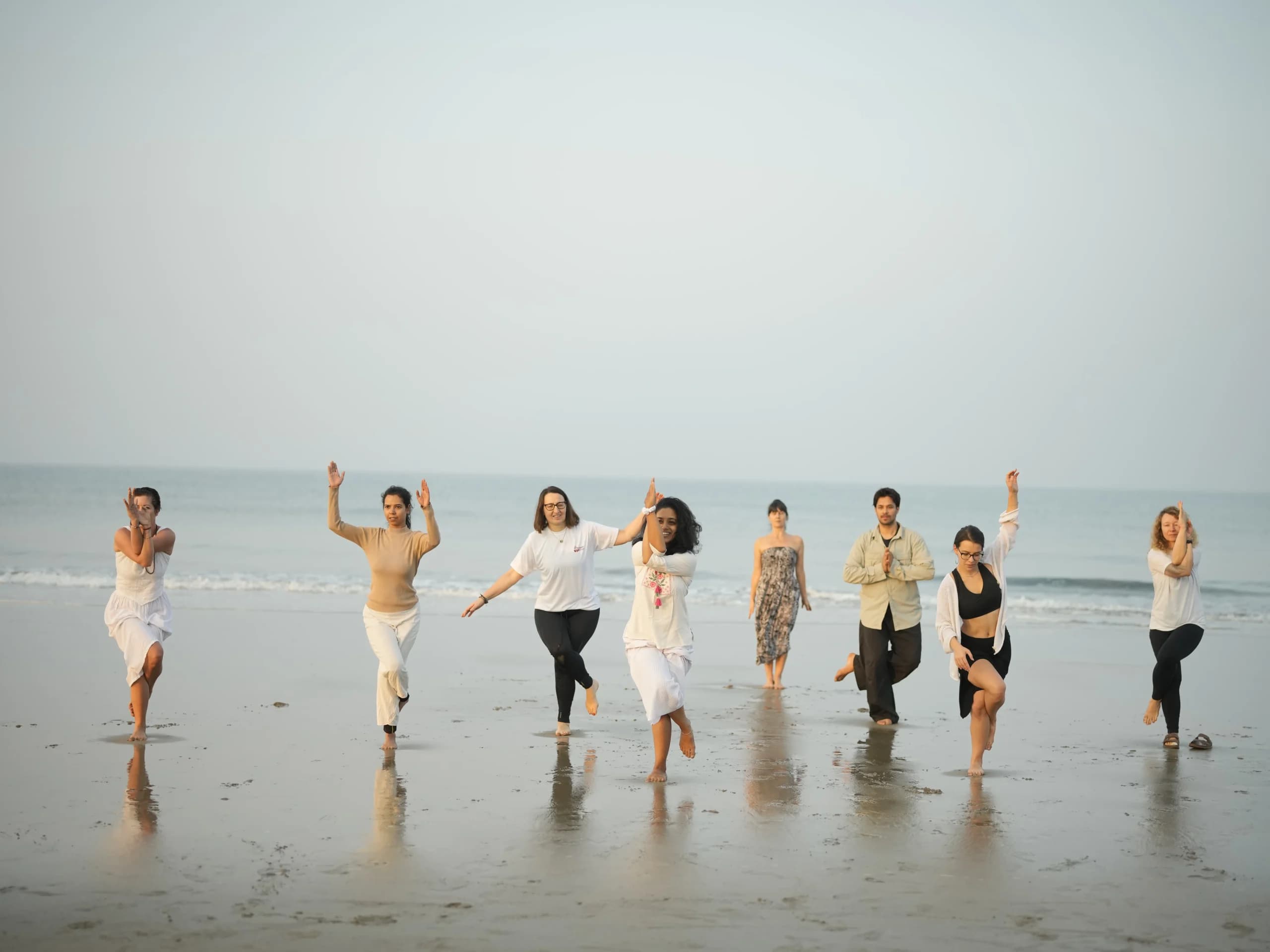 Yoga teacher training group practicing Garudasana (eagle pose) on Arambol Beach, Goa at sunrise