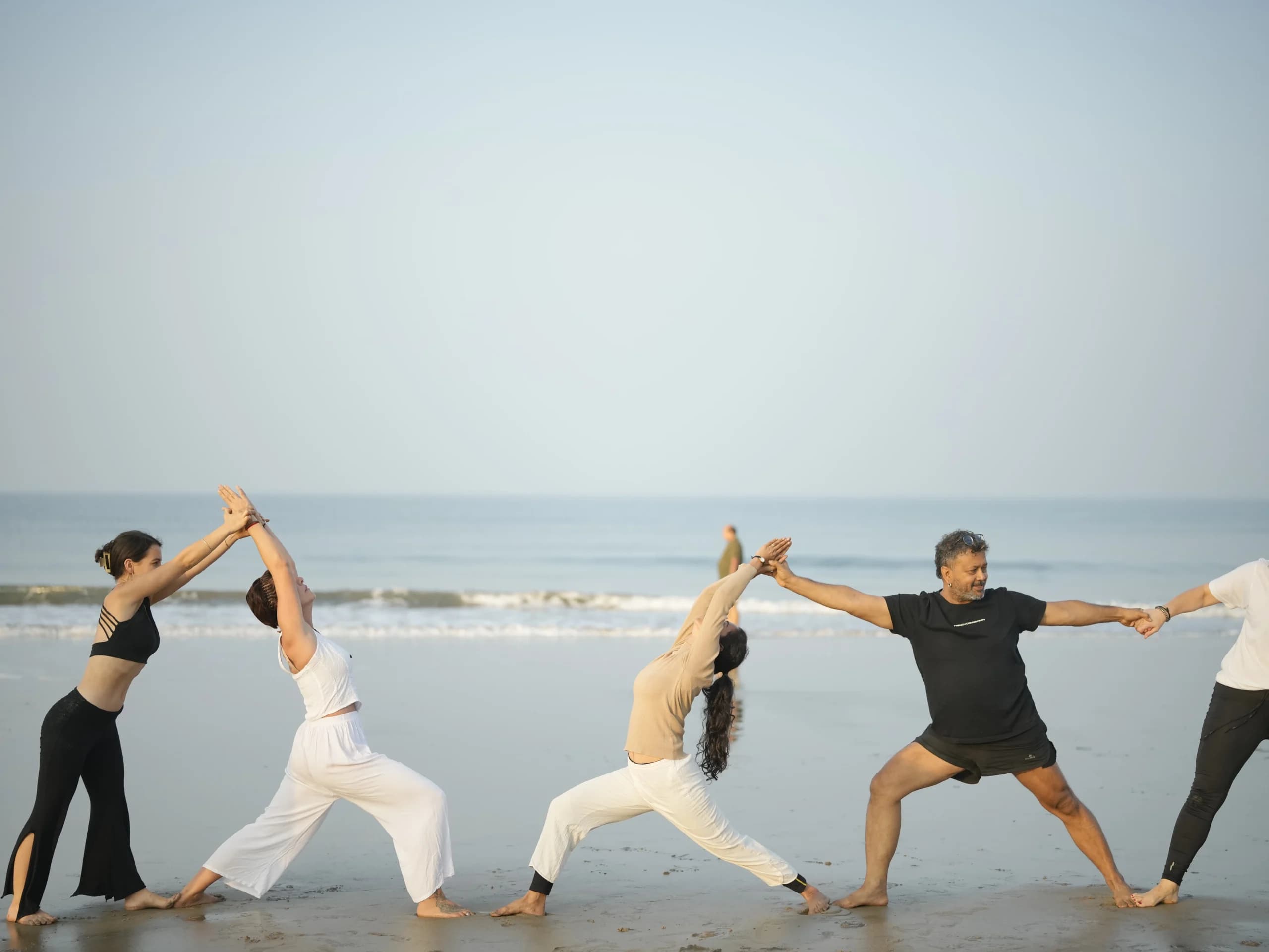 Teacher and students linking hands in Warrior pose sequence on Arambol Beach, Goa