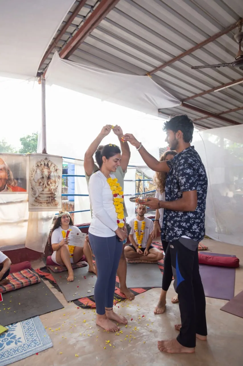 Classmates showering marigold petals over a garlanded student while a teacher holds the puja plate at an Alpesh Yoga graduation ceremony