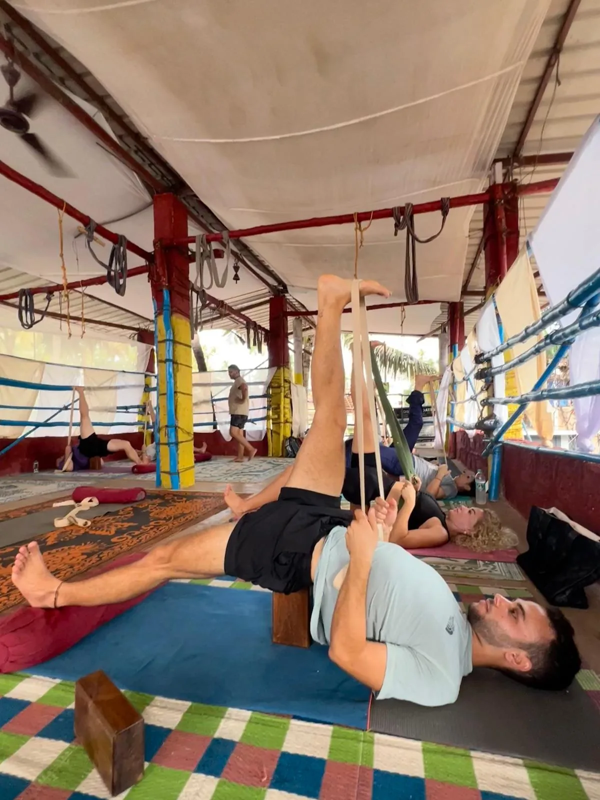Student supported by wall ropes, a bench and blocks in an alignment class at the Arambol shala