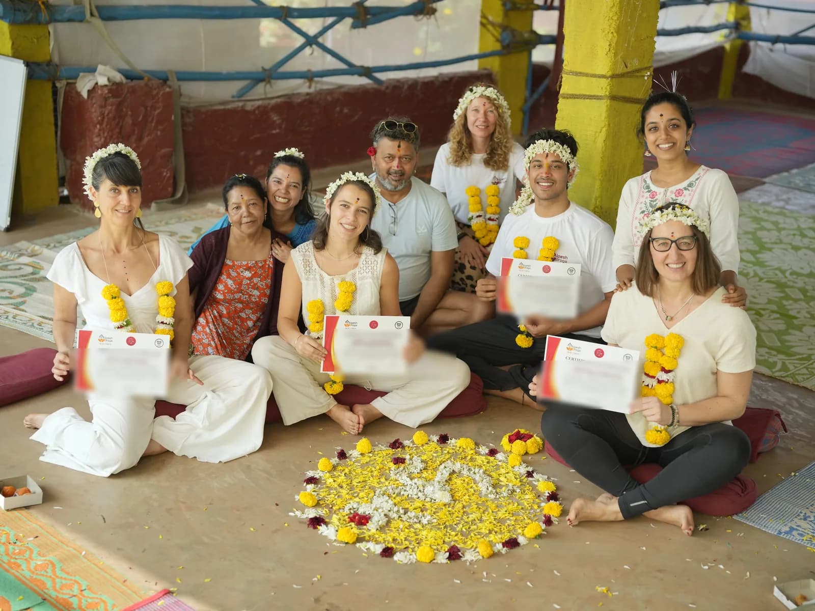 Graduating students holding their Alpesh Yoga certificates of completion, wearing marigold garlands after the closing ceremony