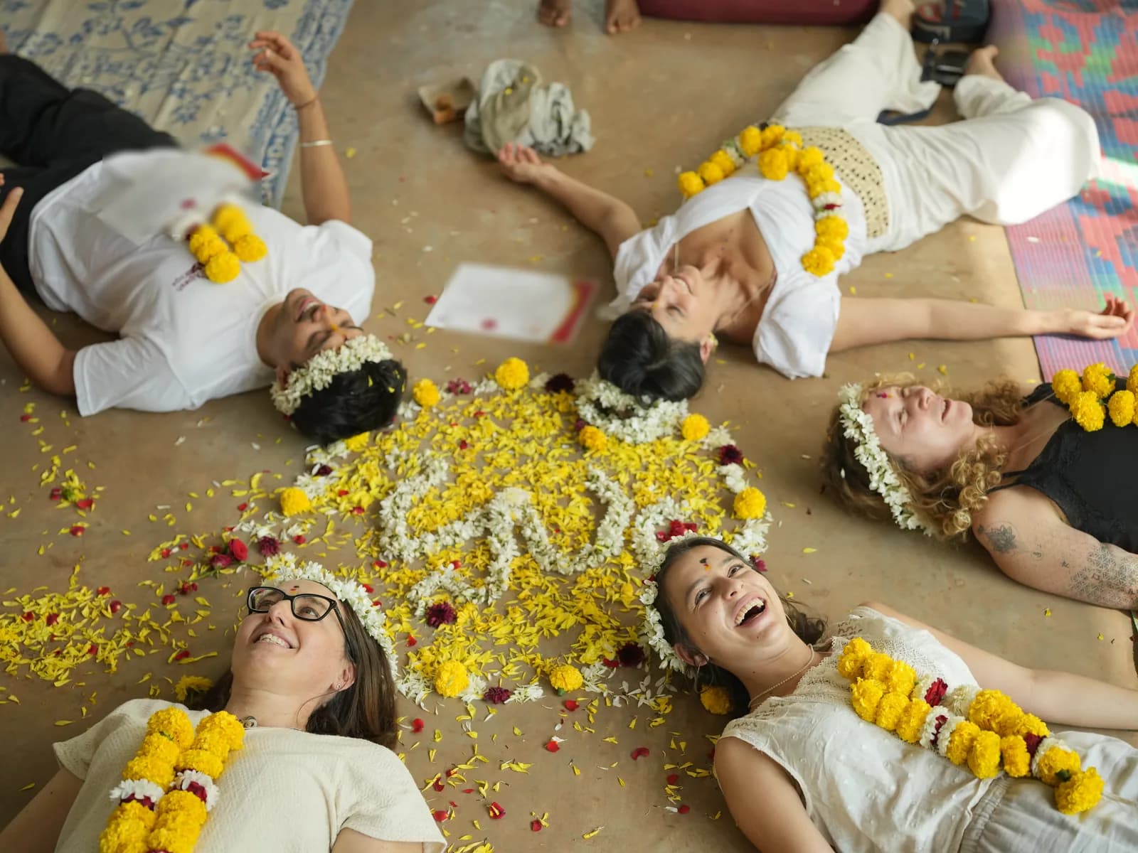 Yoga teacher training graduates lying in a circle around a flower mandala with their certificates after the closing ceremony