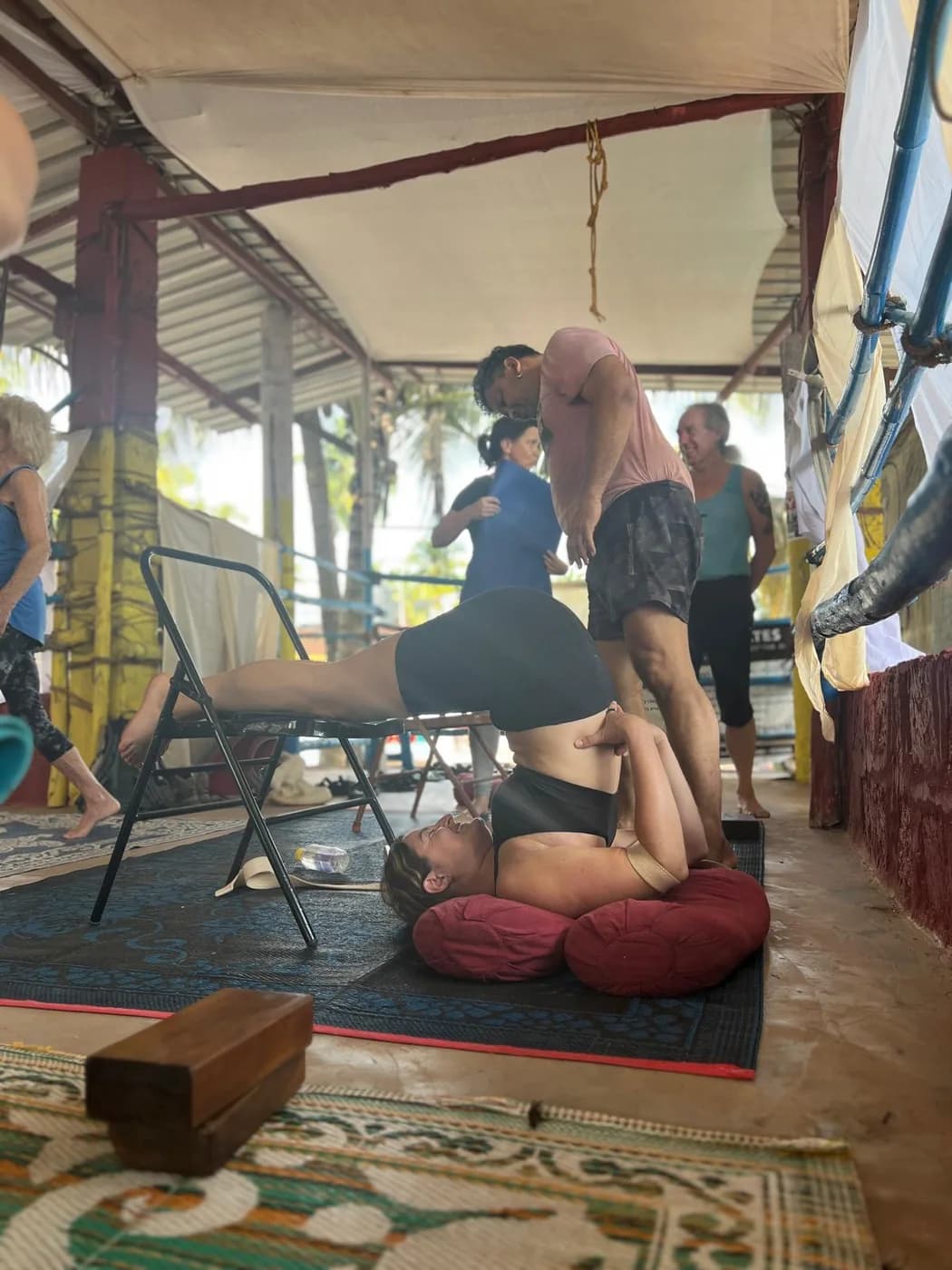 Student in a chair-supported inversion with bolsters under the shoulders, guided by the teacher