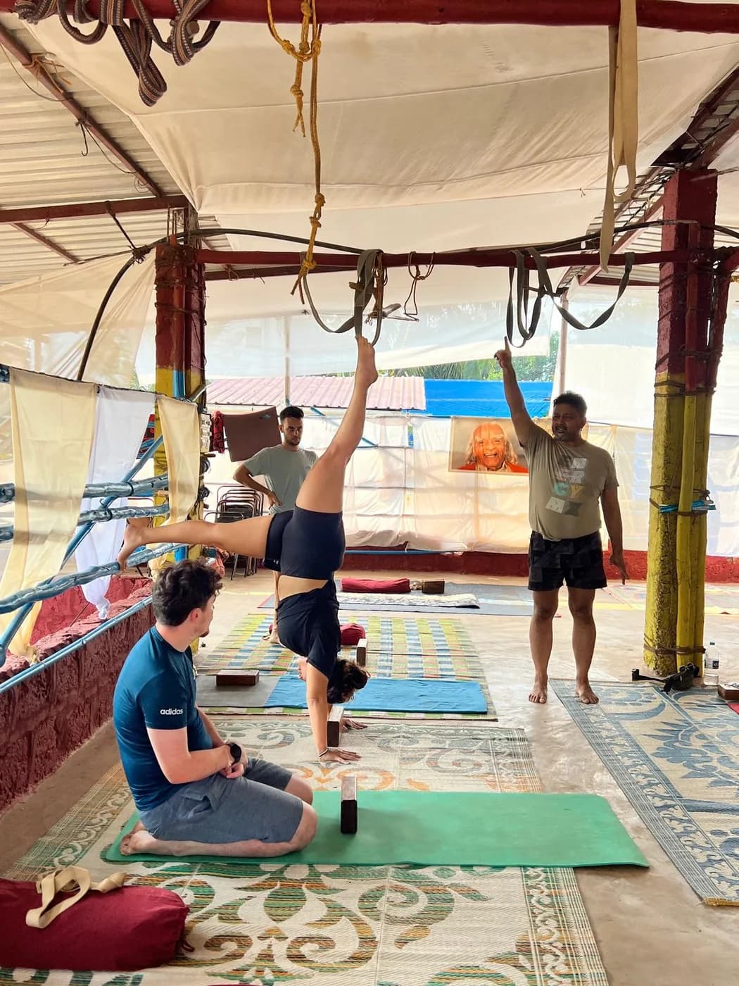Student practising a supported inversion using the shala’s wall ropes while the teacher directs the class