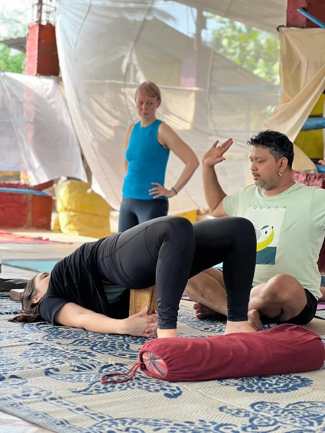 Teacher explaining a supported bridge pose to a student resting on a wooden block