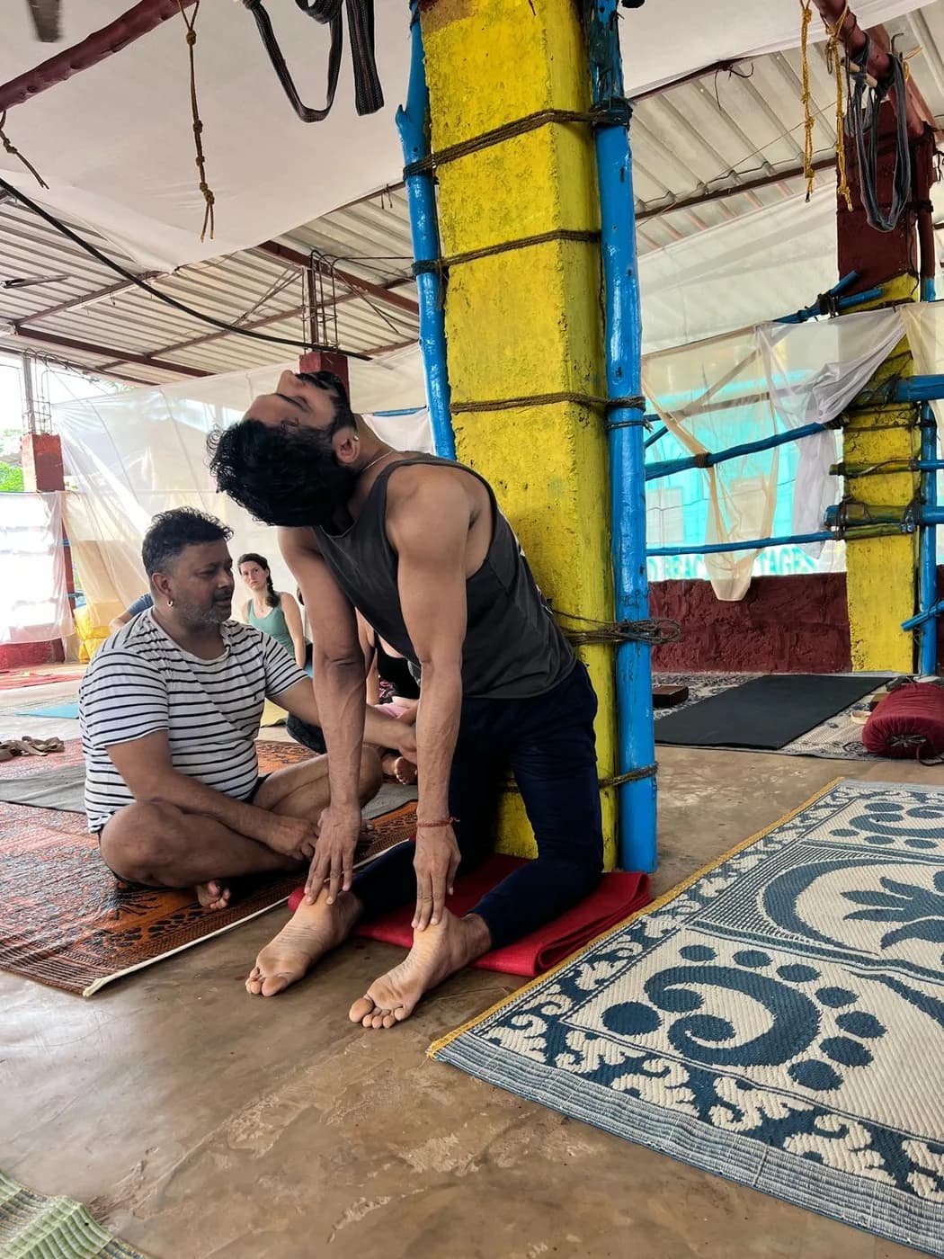 Student in Ustrasana, the kneeling camel backbend, observed by the teacher at the Arambol shala