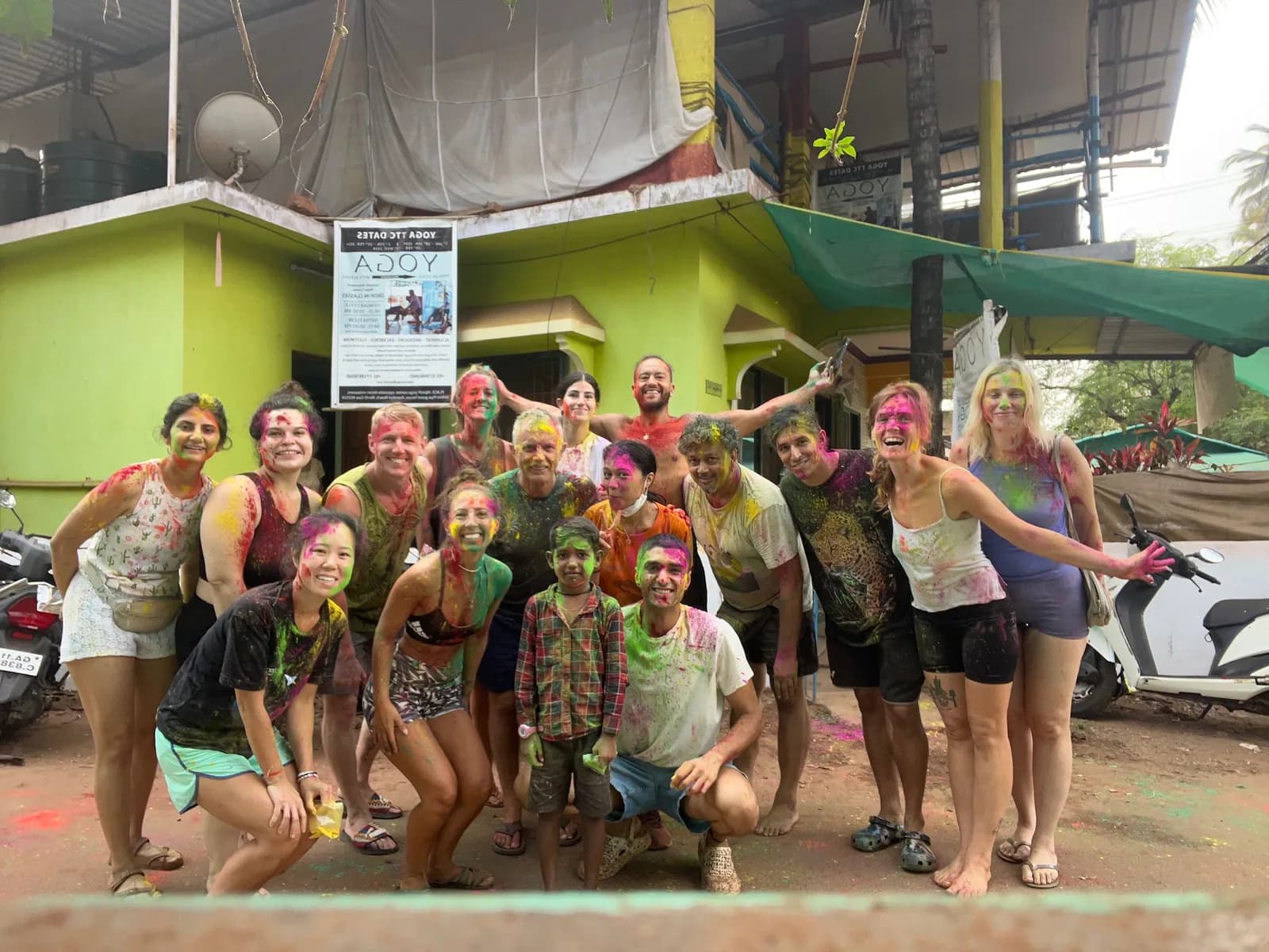International yoga students covered in coloured powder celebrating Holi together outside the yoga school
